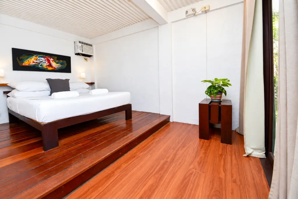 Queen bed with a small side table and plant beside curtained windows