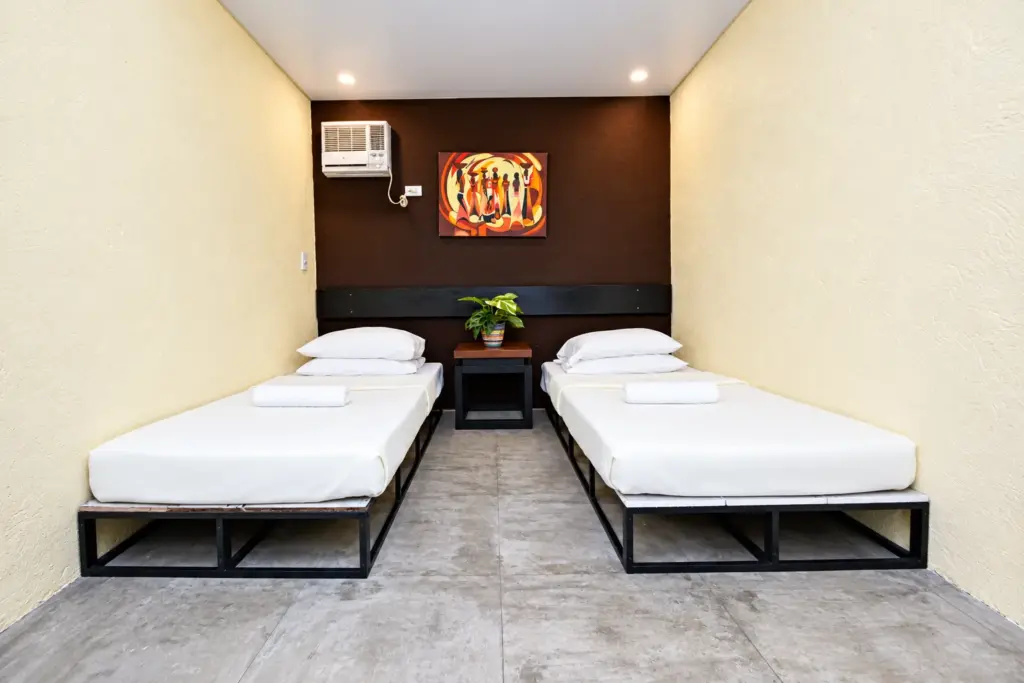 Twin beds on dark frames with an orange artwork behind them