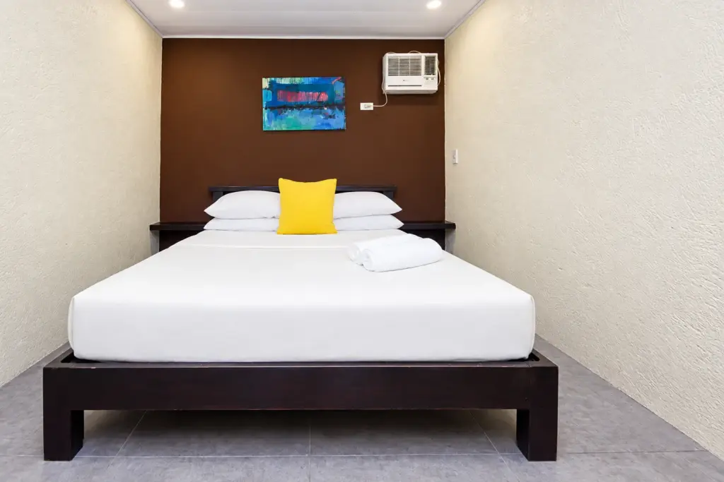 Queen bed with a dark headboard wall, yellow cushion and colorful artwork