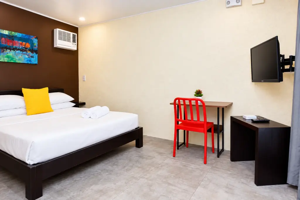 Queen bed with a yellow cushion, red chair and writing desk