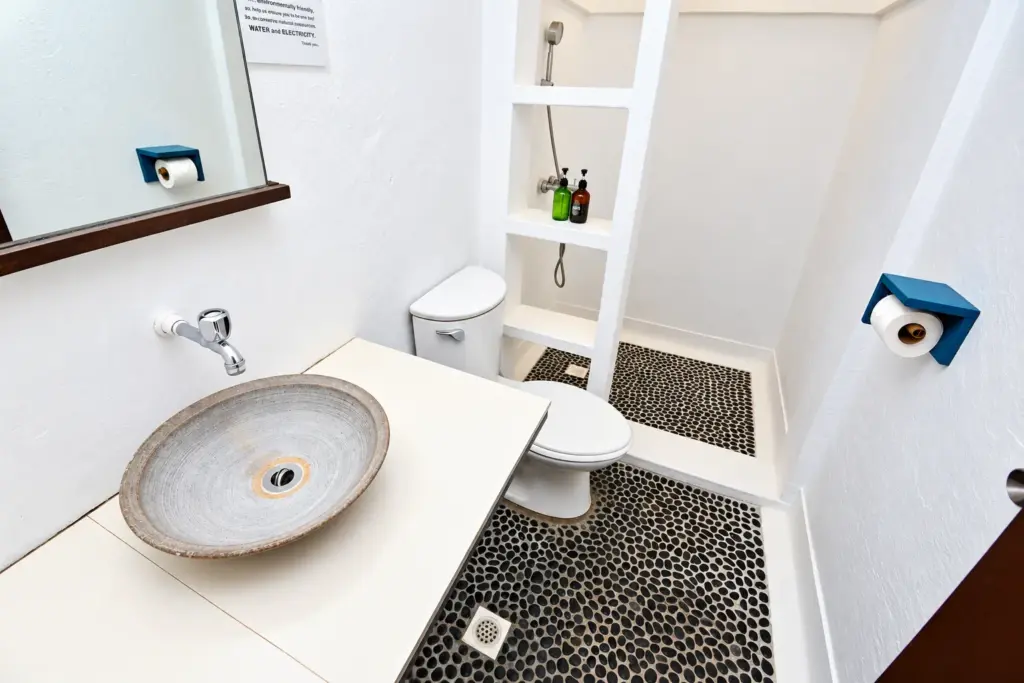 Bathroom with a stone vessel sink, toilet and pebble-floor shower
