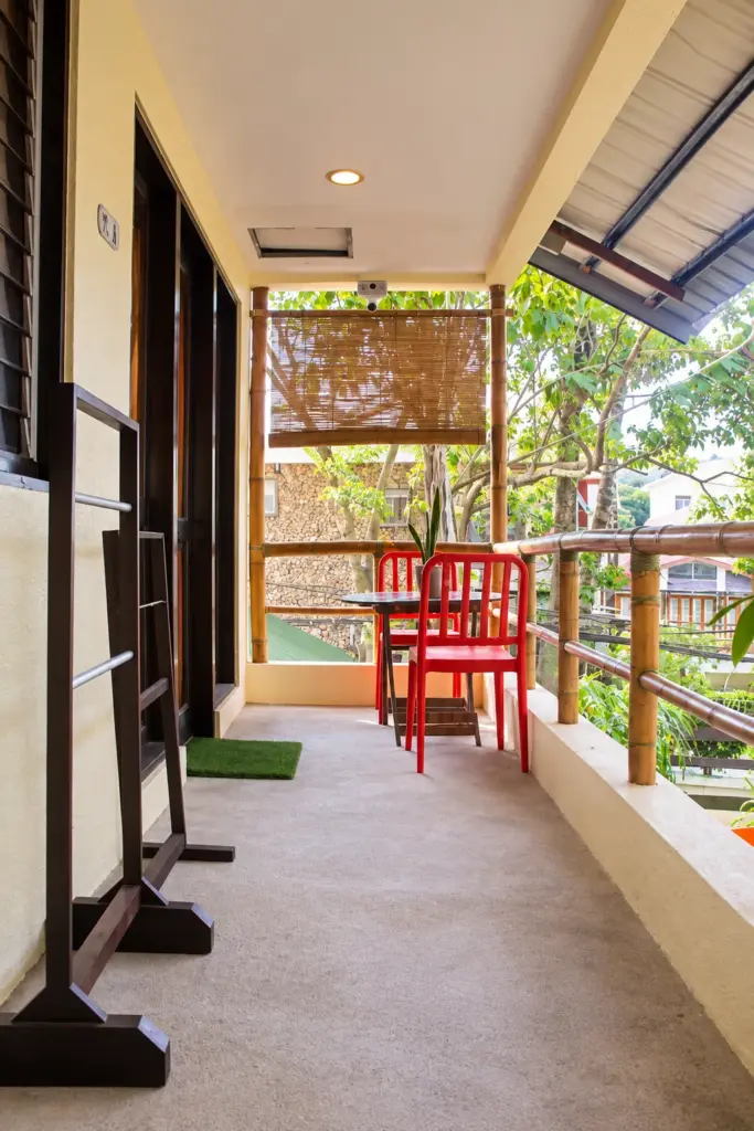 Covered walkway along the dorm balcony with bamboo blinds and a garden view