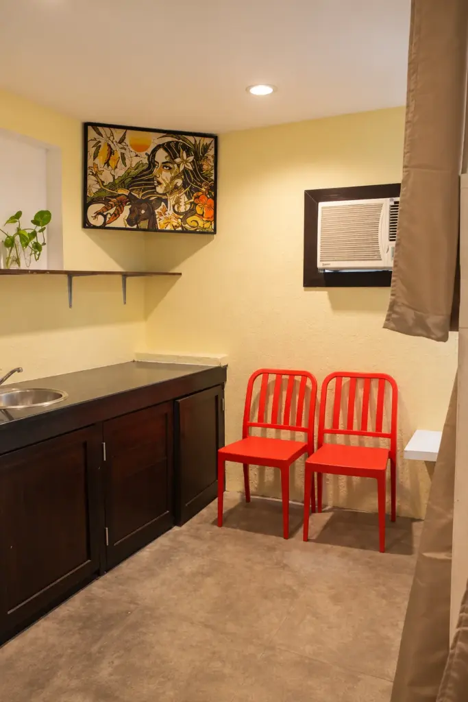 Kitchenette with a sink, two red chairs and local artwork