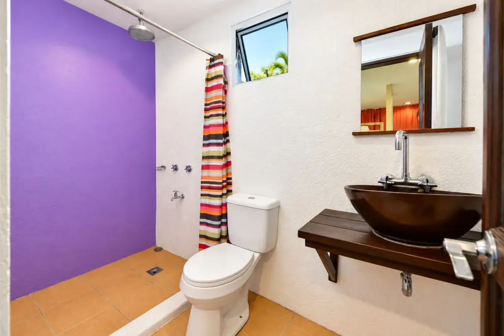 Shared bathroom with a purple wall, bowl sink, toilet and shower