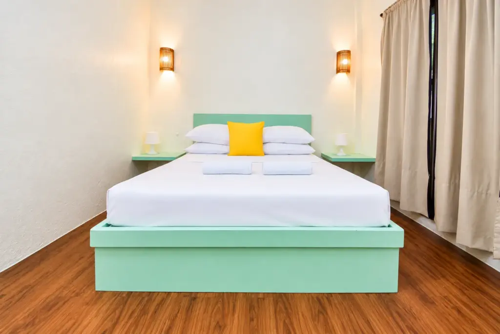 Queen bed with a mint-green frame, white linens and a yellow cushion