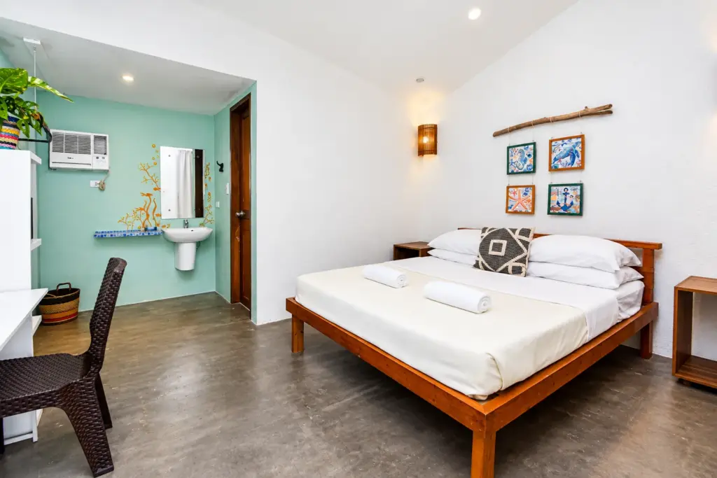 Queen bed with framed prints and a teal bathroom wall
